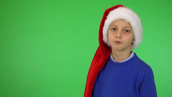 A Young Cute Boy in a Christmas Hat Looks Seriously at the Camera - Green Screen Studio