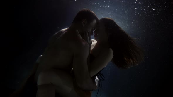 Brunette Lady and Brawny Man Are Hugging Inside Water of Pool Underwater View