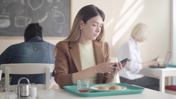Portrait of Young Woman Eating Cutlets in Lunchroom and Answering Phone Call