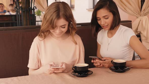 Two young beautiful smiling hipster girls chatting in cafe