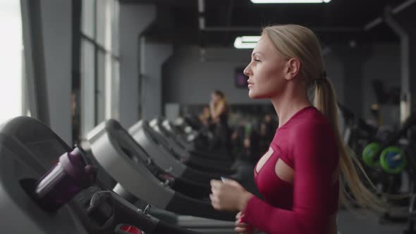 Beautiful Athletic Woman is Jogging in Gym on Treadmill Side View