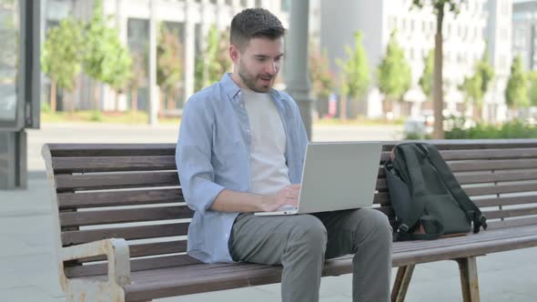 Young Man Celebrating Success on Laptop While Sitting on Bench