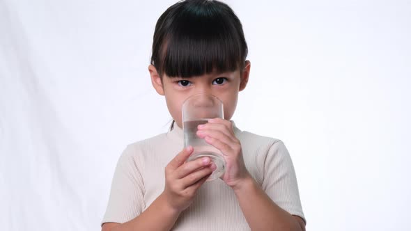 Cute little asian girl drinking water from a glass on white background in studio.