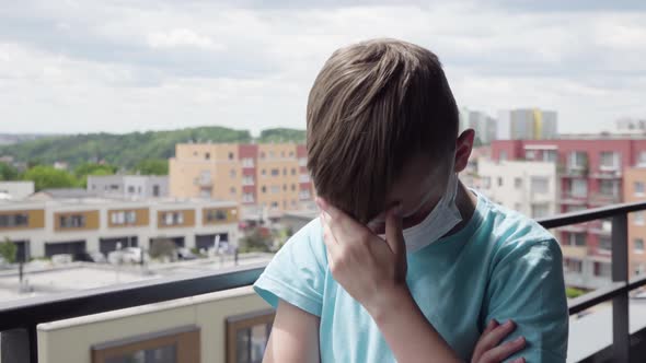 A Young Boy in a Face Mask Stands on a Balcony, Looks Over the Cityscape Below and Then Acts Upset