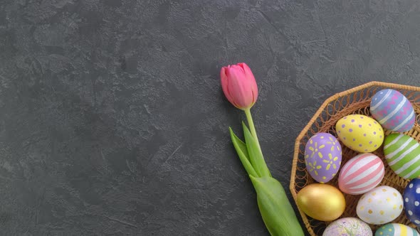 Hand Putting Down Tulips Next to Colorful Easter Eggs in Basket on Bright Background