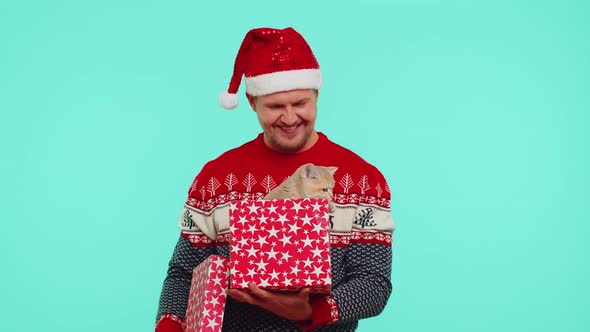 Man in Christmas Red Sweater Hat Smiling Unwrapping Gift Opening Box with Pet Cat Great Surprise