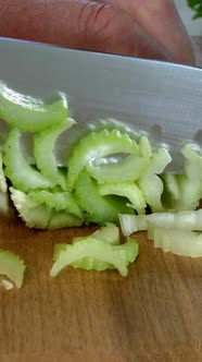 Chef Hands Chopping Celery Stem Into Small Slices with Kitchen Knife on Wooden Kitchen Board