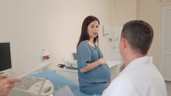 Beautiful Pregnant Woman in Denim Dress Sitting at Medical Cabinet During