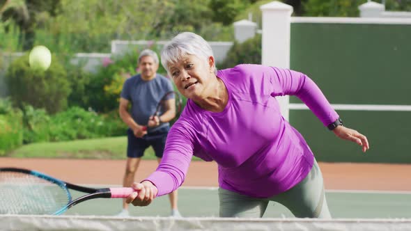 Video of happy biracial senior woman practicing tennis on tennis court