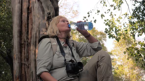 Woman Tourist Was Leaning Back Against A Tree And Drinking Water From Bottle