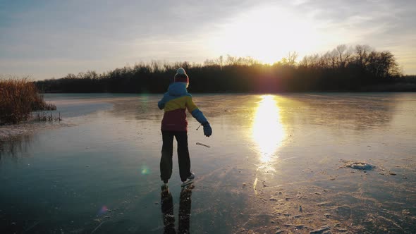 Cute Little Girl Is Going Skate Outdoors at Sunset. A Schoolgirl Enjoying Ice Skating at Frozen Lake