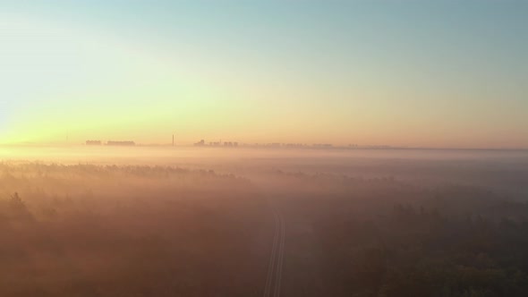 Aerial view of a foggy autumn forest with a railway at sunrise.