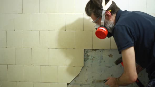 Worker in Respirator and Protective Glasses with Hammer and Spatula Dismantles an Old White Dirty