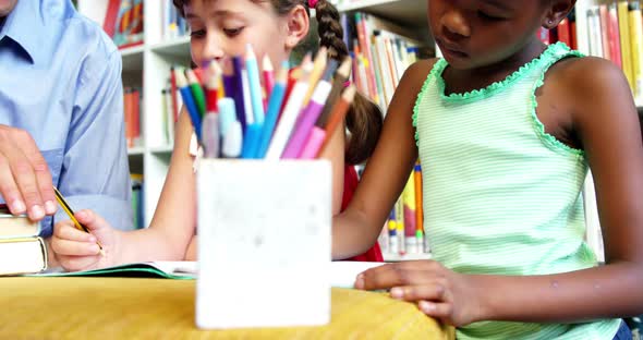 Teacher helping schoolkids with his homework in library at school