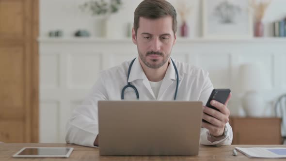 Young Doctor Using Smartphone While Using Laptop in Clinic