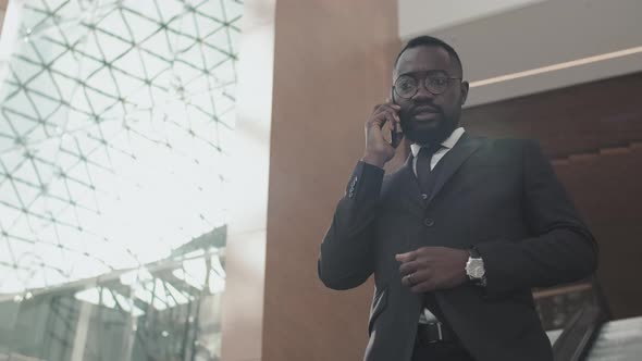 Businessman Talking on Phone and Going Down Escalator