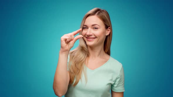 Disappointed Young Woman Showing Small Size Gesture Against Blue Background