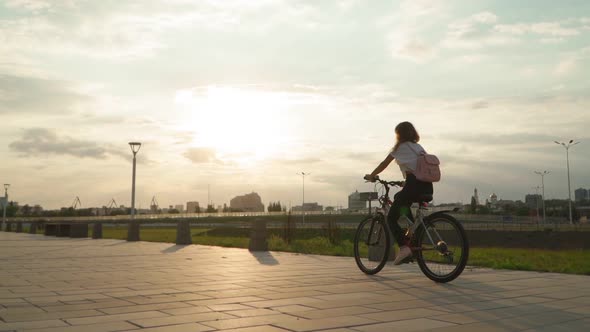 woman rides a bicycle during sunset. Cyclist girl with pink backpack on her back