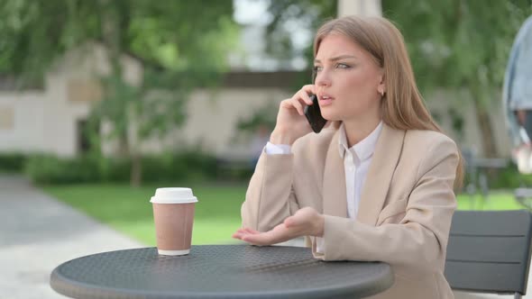Angry Young Businesswoman Talking on Phone in Outdoor Cafe