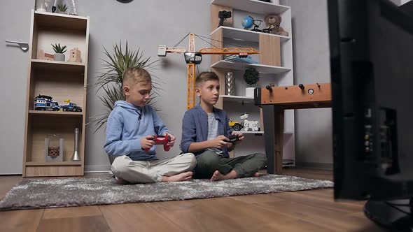 Teenage Brothers Sitting on the Carpet and Competing in Video Game Using Gamepads