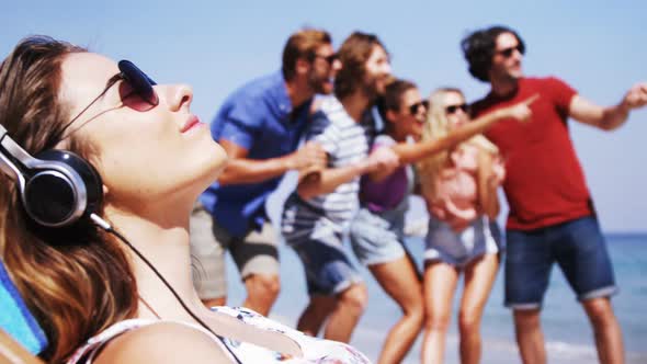 Beautiful woman listening to music while friends taking a selfie at beach