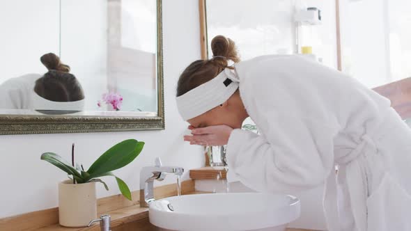 Woman in bathrobe washing her face in the sink