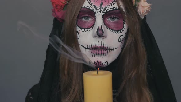 Woman in the Image of Death Santa Muerte or Sugar Mexican Skull Puts Out a Candle in Her Hands on a