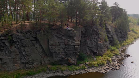 A Guy and a Girl are Sitting on a Steep Cliff Waving to a Drone That Has Come to Them