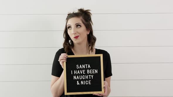 Up close of woman holding sign saying, Santa I have been Naughty and Nice