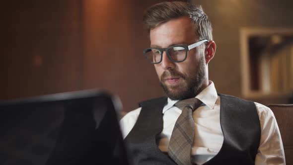 Young Businessman in Glasses Working at a Laptop Man in the Suit Sitting on the Couch in the Hotel