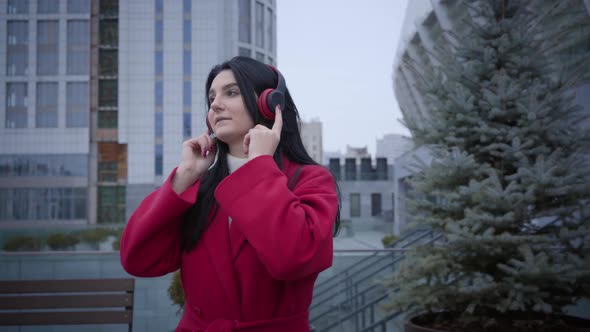 Portrait of Cheerful Cute Girl in Red Coat Walking and Dancing As Listening To Music in Earphones