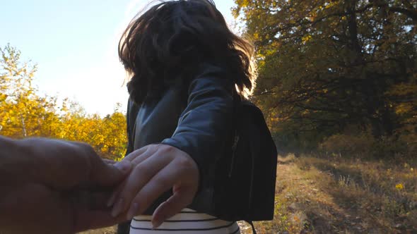 Follow Me Shot of Happy Girl Leads Her Boyfriend Along Trail Near Autumn Forest. Young Woman Holds