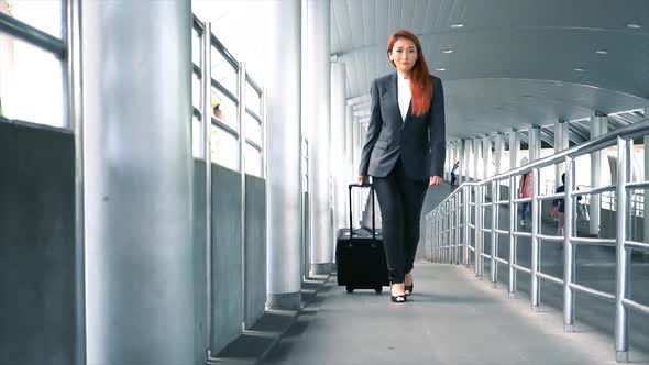 Young Attractive Asian Business Woman Dragging a Wheeled Suitcase at the Airport for Business Trip