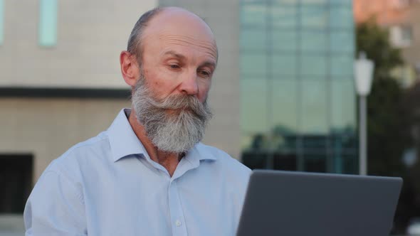 Closeup Pensive Elderly Man with Gray Beard Sitting Outdoors Using Laptop