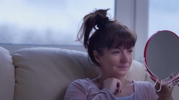 Happy Woman Sits on the Sofa and Looks in the Mirror, Admires Appearance