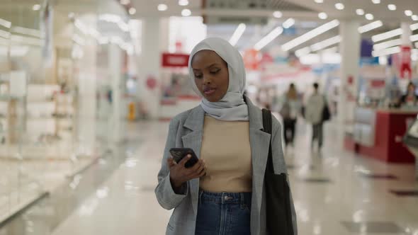 Black Woman in Hijab Looks at Phone Smiles with News in Mall