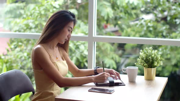 Young pretty woman writing in appointment book at coffee shop