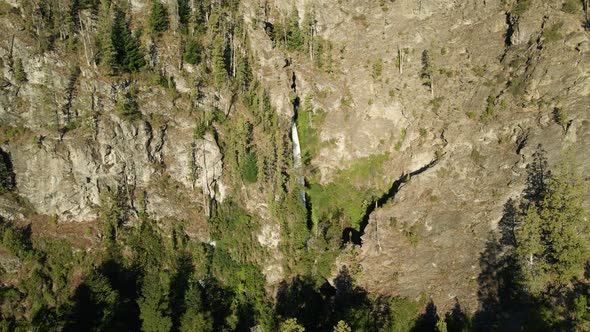 Aerial jib up of Corbata Blanca waterfall flowing between steep mountains with cypress trees, Patago