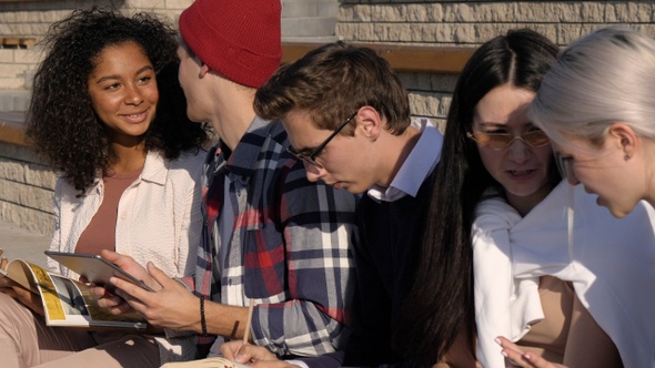 Multi-ethnic students hanging out outdoors doing some homework.