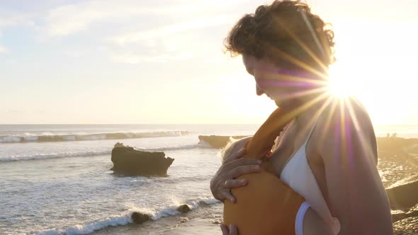 Young White Mother Breastfeeding Her Child Watching the Ocean on a Sunrise