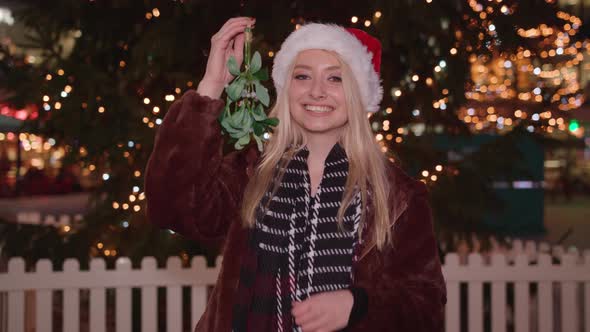 Beautiful woman blows you a kiss whilst holding mistletoe