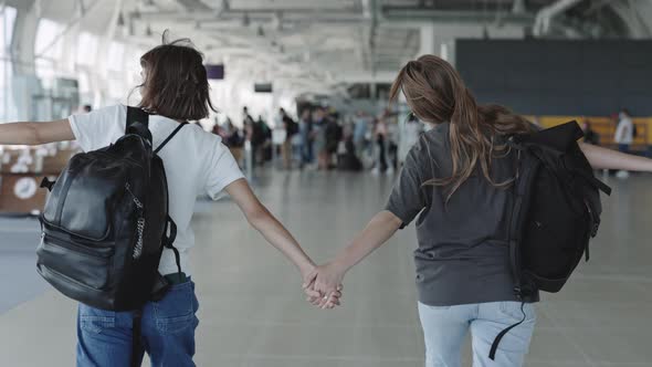 Two Carefree Lesbias Holding Hands and Running at Airport