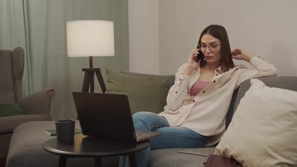 Beautiful Woman During a Break Talking on the Phone Sitting on the Sofa in the Living Room