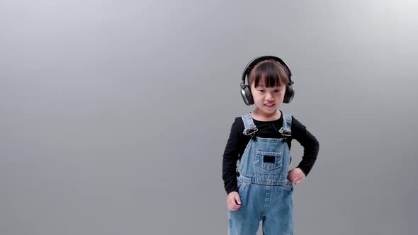 Little asian girl wearing headphones listening to music and dancing in studio.