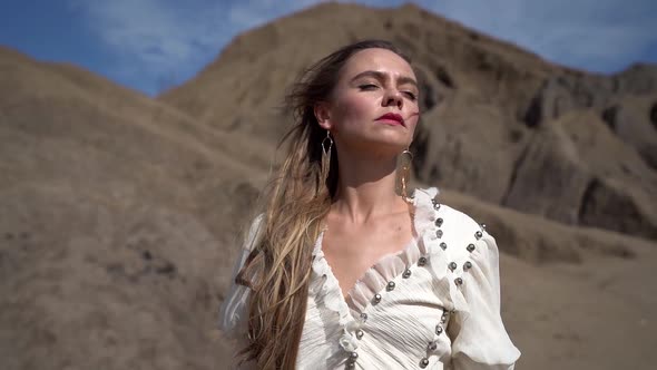 Sensual Woman Is Standing at Wind Near Dry Sandy Rocks, Free and Lonely, Listening To Nature