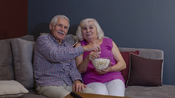 Portrait of Elderly Couple Watching TV at Home Eating Popcorn Enjoying Film Together at Home