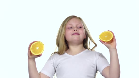 Little Girl Holding an Orange Slice Closes Her Eyes and Curves. White Background. Slow Motion