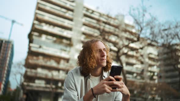 Meditative curly-haired man looking at mobile