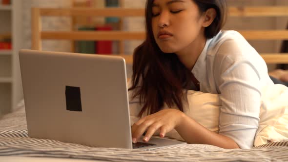 Portrait of Bored Young Asian Girl Lying Down on Bed While Working From Home in Bedroom