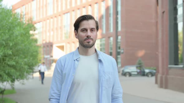 Serious Man Walking in Street While Looking at Camera